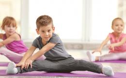 Dzieci na sali gimnastycznej rozciągające nogi w siadzie.