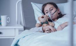 Dziecko w masce tlenowej na szpitalnym łóżku. Przytula misia.