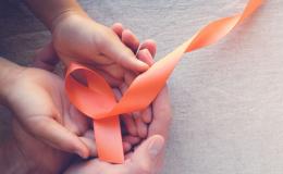 Pomarańczowa  wstążka leży na dłoniach dziecka, a one leżą na dłoniach dorosłej osoby