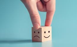 Drweniana kostka, na jednej ściance jest smutna buźka, na drugiej uśmiechnięta.