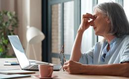 Kobieta przy laptopie, uciskająca jedną ręką oczy.