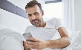 Leżący w łóżku facet patrzy na swój telefon