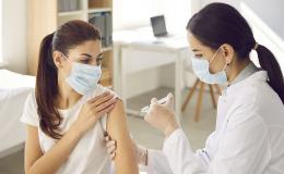 Pielęgniarka wykonuje kobiecie zastrzyk, obie w maseczkach