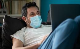 Mężczyna leży na kanapie z laptopem na kolanach i umawia się na test covid przez internet.