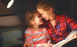 Uśmiechnięte młoda matka i córka w wieku wczesnoszkolnym. Siedzą i wspólnie czytają książkę.