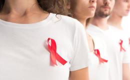 Osoby w białych koszulkach z przypiętą do piersi czerwoną wstążeczką