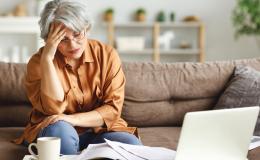 Kobieta na kanapie przed laptopem, podpierająca głowę ręką w geście przytłoczenia