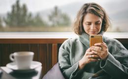 Kobieta w dresie patrzy na komórkę, przed nią kawa