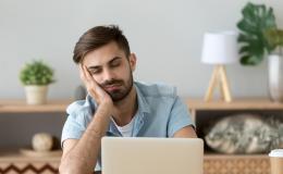 Mężczyczna przed laptopem, głowa podparta na dłoni.