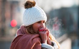 Kobieta w białej czapce, chuchająca w ręce, żeby się rozgrzać