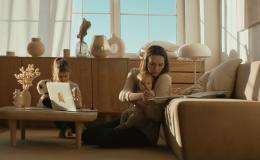 Kobieta siedzi na podłodze przy kanapie z małym dzieckiem, starsze dziecko bawi się na stoliku