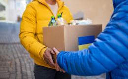 Ktoś przekazuje paczkę z żywnością. Na pudełku jest flaga Ukrainy.