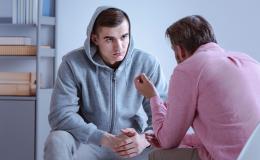 Młody chłopak siedzi i rozmawia z terapeutą. Ma na sobie dres, a na głowie kaptur.