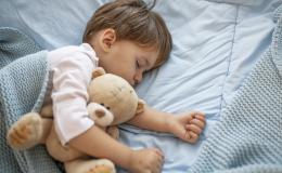 Mały chłopczyk śpi pod kocem. Przytula się do misia.