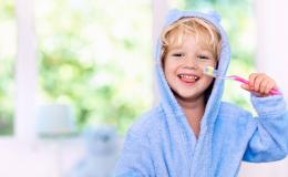 Kilkuletni chłopczyk w szlafroku trzyma szczoteczkę do zębów. Wystawia język, widać mu zęby mleczne.