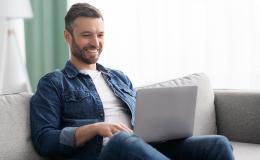 Uśmiechnięty mężczyzna z laptopem na kolanach