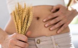 Zbliżenie na goły brzuch kobiety. W jednej ręce trzyma kłosy zbóż, a drugą dotyka brzucha.