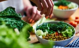 Kobieca ręka posypuje posiekanym koperkiem zielone warzywa w misce.