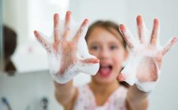 Mała dziewczynka wyciąga ręce do przodu i pokazuje namydlone dłonie.