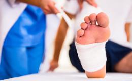 Mężczyzna podczas wizyty u ortopedy. Na zbliżeniu widać jego stopę owiniętą bandażem.