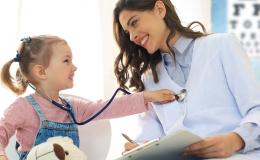 Mała dziewczynka podczas wizyty kontrolnej u lekarza. Na kolanach ma misia, na szyi stetoskop, którym bada lekarkę. Obie się uśmiechają