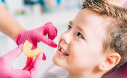 Chłopiec podczas wizyty u ortodonty. Lekarz w różowych rękawiczkach zbliża wycisk do jego ust.