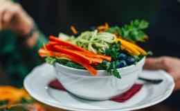 Kelner podaj danie na talerzu. Jest na nim papryka, marchewka, borówka amerykańska, pieruszka, zielony makaron.