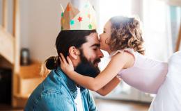 Córeczka w stroju baletnicy całuje ojca w czoło. Mężczyzna ma na głowie papierową koronę.