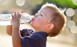 Kilkuletni chłopiec w upalny dzień pije wodę z buletki.