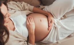 Leżąca kobieta w ciąży obejmuje brzuch dłońmi.