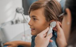 Chłopiec podczas wizyty u laryngologa. Lekarka bada mu ucho otoskopem.