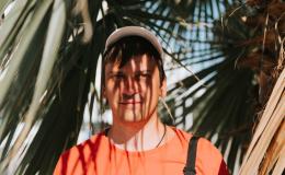 Mężczyzna w czpace z daszkiem w cieniu rzucanym przez liście palmy. Widok twarzy i liści.