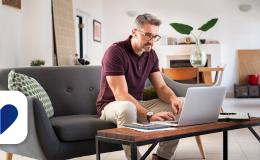 mężczyzna pisze coś w komputerze stojacym na "jamniku" przy kanapie 