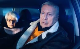 Starsza para w aucie nocą. Mężczyzna za kierownicą jest zmieszany, kobieta lekko wystraszona.