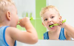 Mały chłopiec myjący zęby w łazience. Odbicie w lustrze.