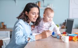 Mama z dzieckiem przy stole. Mama przegląda telefon, a dziecko bawi się klockami.