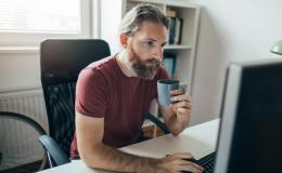 Brodaty mężczyzna z kubkiem przed laptopem