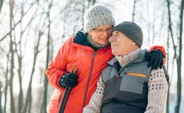 Starsza para na zimowym spacerze, on siedzi, ona go obejmuje