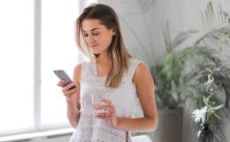 kobieta ze szklanką wody i komórką, w białym podkoszulku