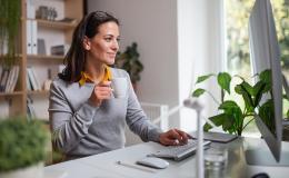 Kobieta z kubkiem kawy w domu przed komputerem