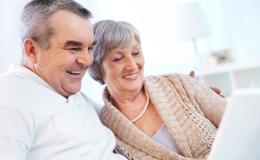 Starsza para z uśmiechem patrzy na ekran laptopa