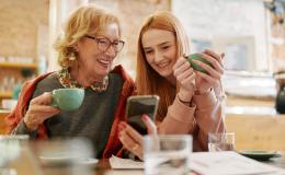 Babcia i wnuczka patrzą na telefon komórkowy, pijąc herbatę w kuchni