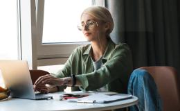 Blondynka w okularach przy laptopie leżącym na stoliku koło okna