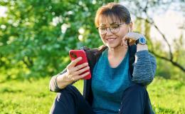 Pani siedząca na trawie z uśmiechem patrzy na telefon