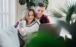 uśmiechnięta para młodych na kanapie przed laptopem