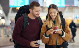 mlodzi ludzie na lotnisku z plecakami patrza na telefon