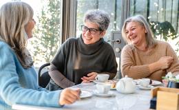 trzy kobiety w średnim wieku przy wspólnym stole, jedna patrzy na komórkę