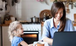 Uśmiechnięta matka przed laptopem, obok smieje się kilkuletnia córka