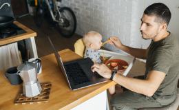 ojciec karmi dziecko łyżeczką i patrzy w laptop