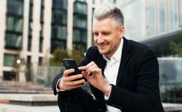 Mężczyzna w garniturze z telefonem siedzi przed biurowcem